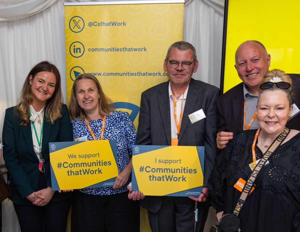A group of people standing together at a Communities That Work event, holding signs showing their support.
