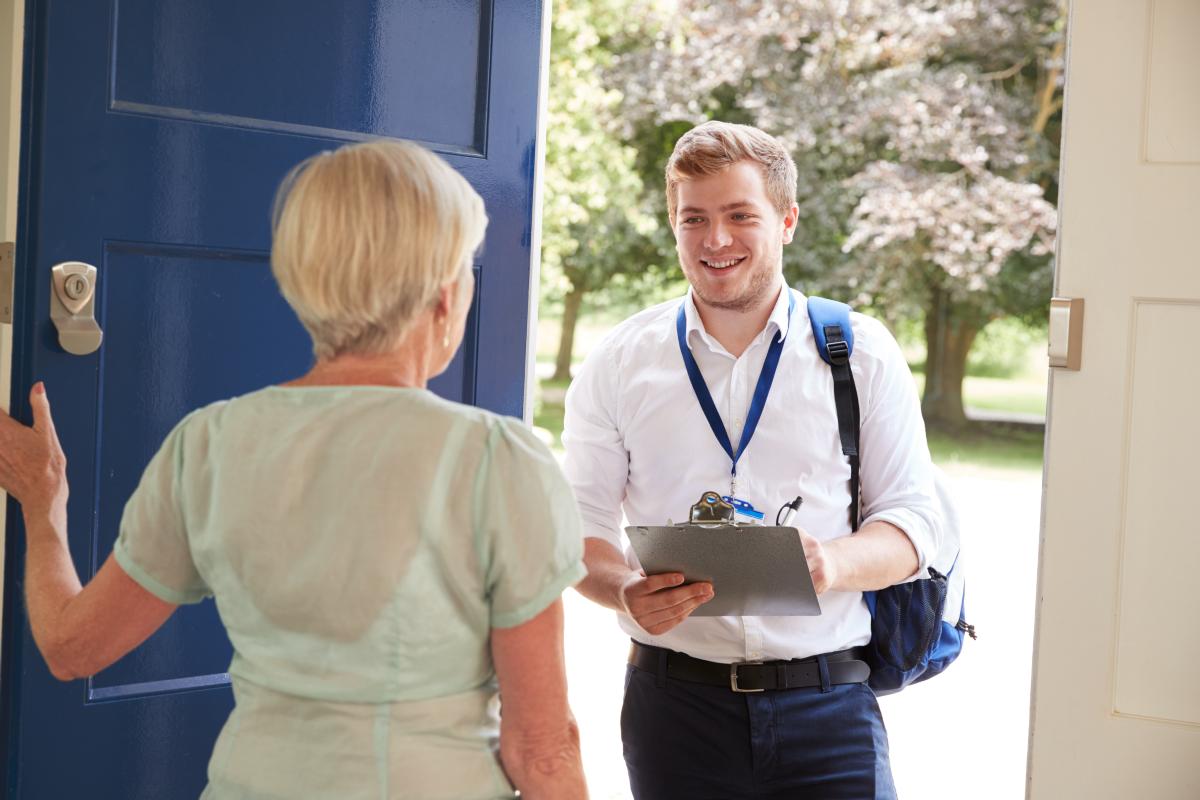 A doorstep conversation between two people, with one holding a clipboard and wearing an ID lanyard.