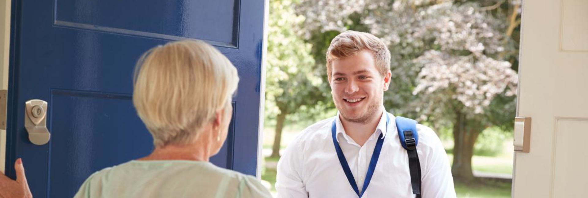 A doorstep conversation between two people, with one holding a clipboard and wearing an ID lanyard.