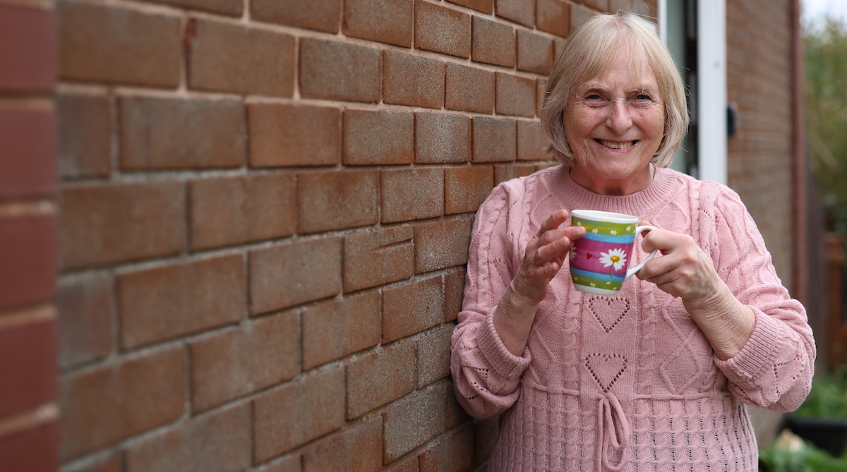 Someone holding a patterned mug while leaning against an exterior brick wall.