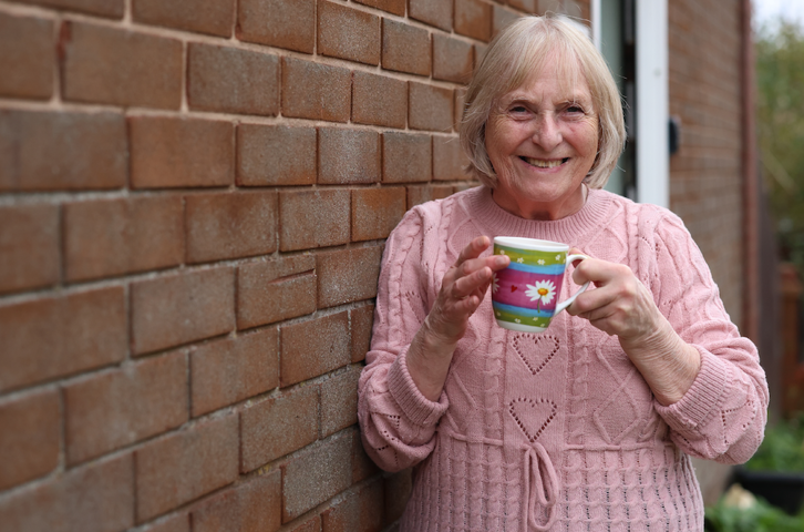 Someone holding a patterned mug while leaning against an exterior brick wall.