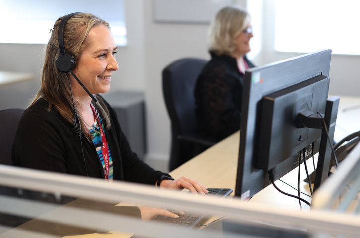 Two colleagues at desks using computers and headsets in a call‑handling team.