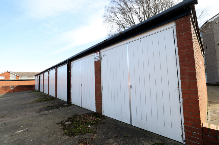 Line of garages with white doors and a paved area in front.