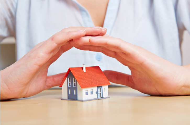 A pair of hands forming a shelter over a miniature house to show protection.