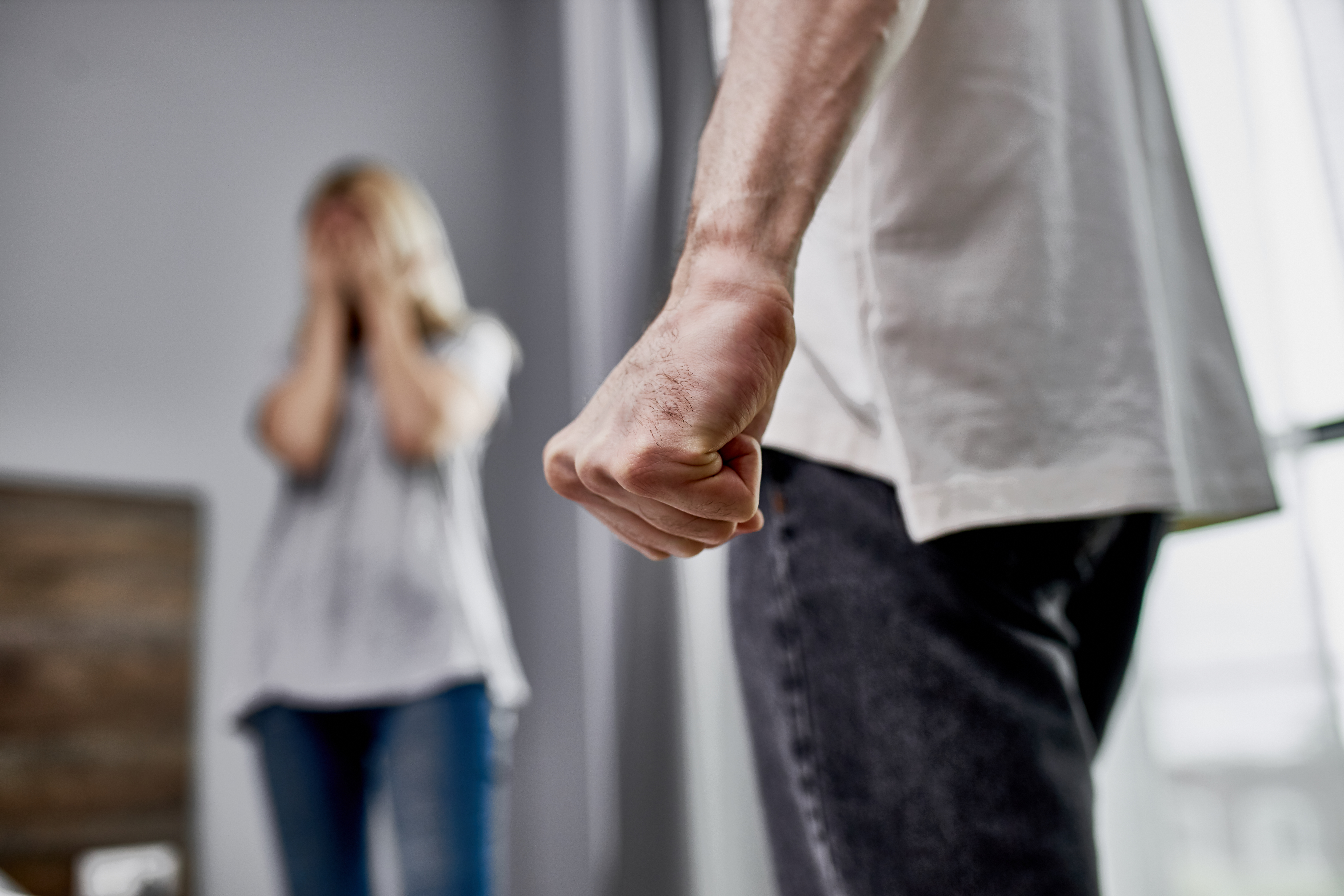 A person standing with a clenched fist in the foreground while another person stands further back covering their face.