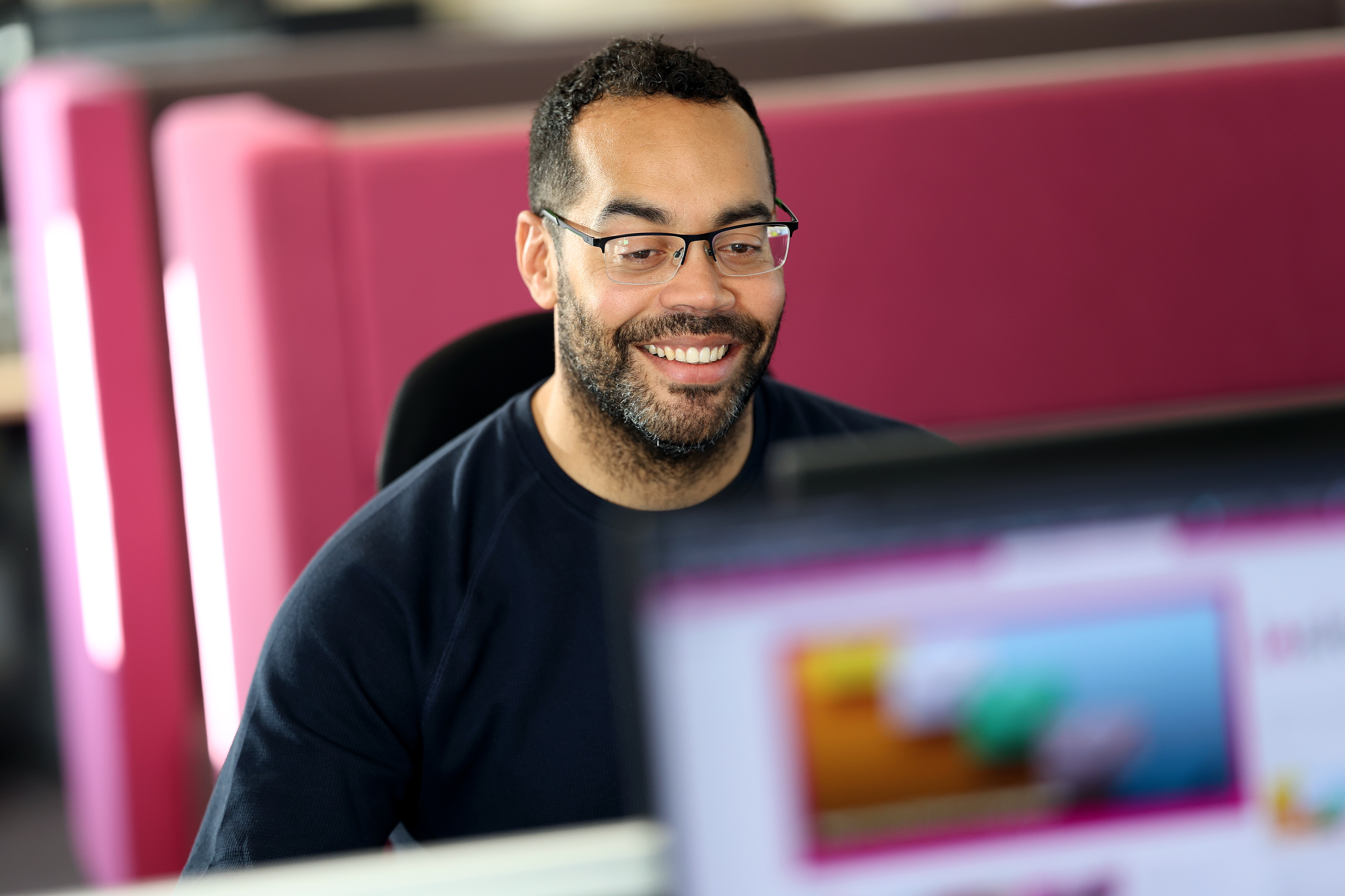 A colleague working at a computer in a bright office with pink dividers.
