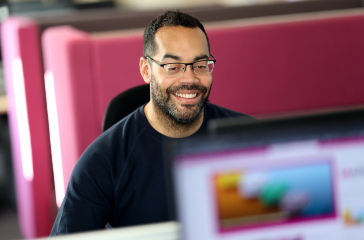 A colleague working at a computer in a bright office with pink dividers.