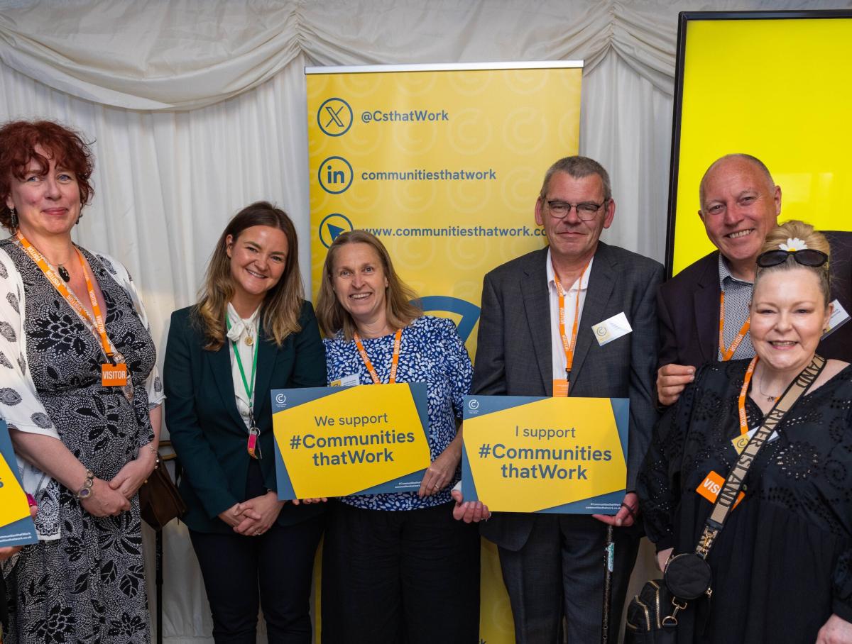 A group of people standing together at an event holding signs that show support for the Communities that Work campaign.