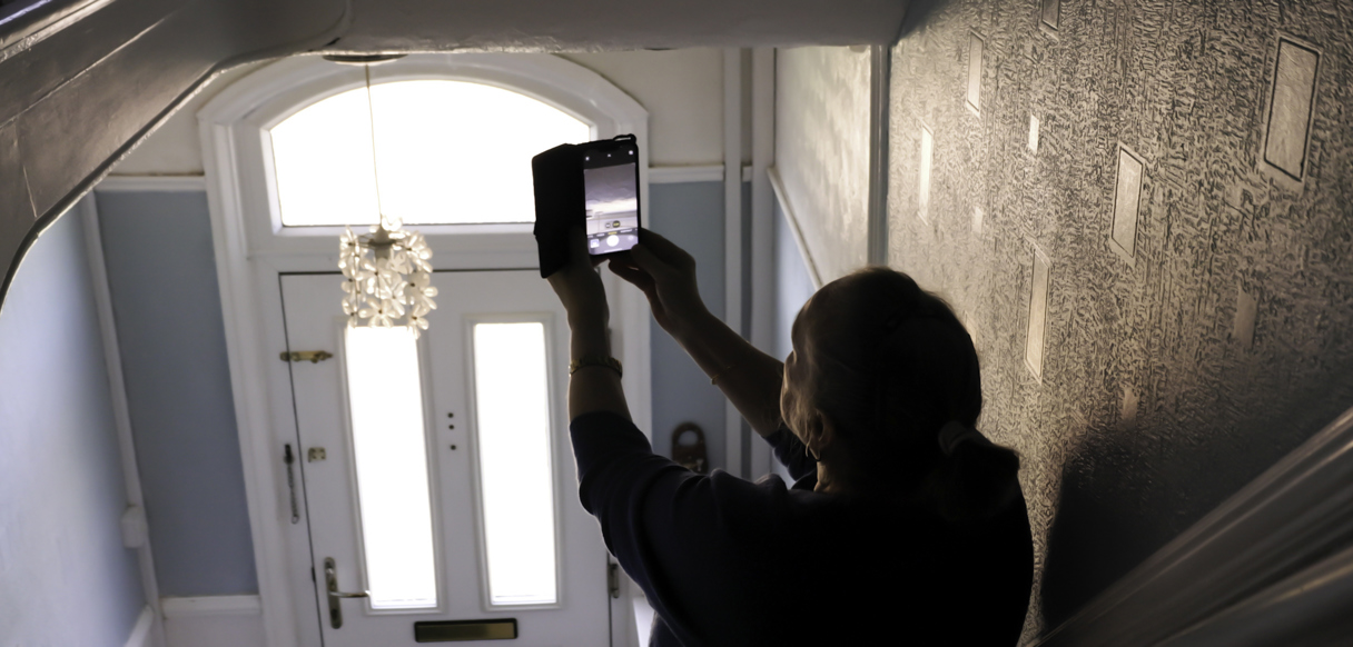 Customer holding up a phone to capture an issue in their hallway for a repairs request.