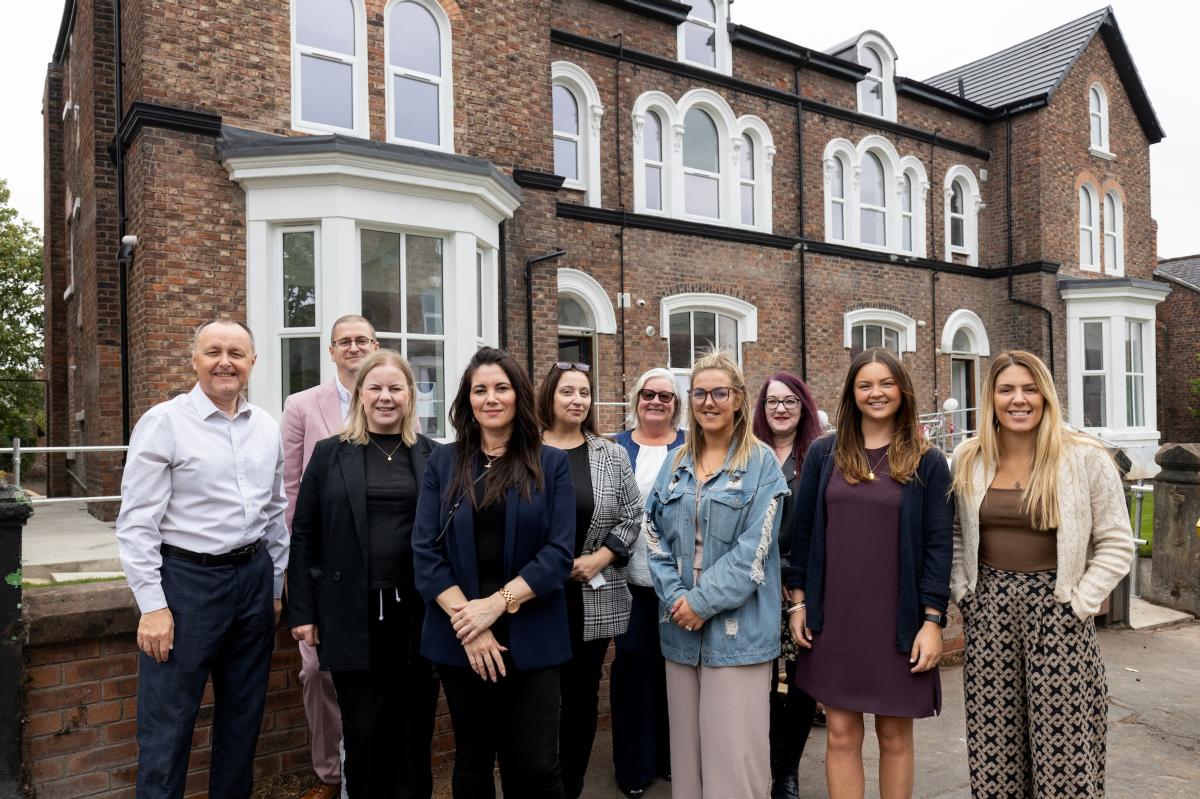 A group of people standing together outside a large brick building that now offers specialist supported housing.