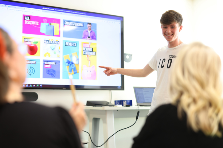Image of young man smiling and pointing at a presentation on screen