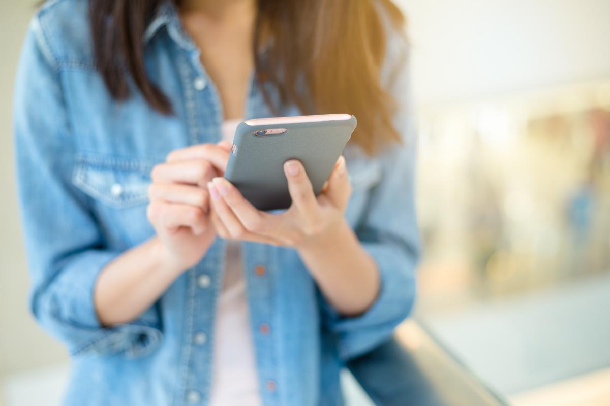 A person using a smartphone, holding it with both hands while standing indoors.