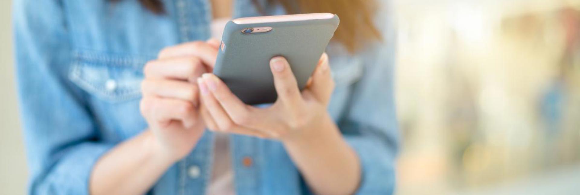 A person using a smartphone, holding it with both hands while standing indoors.