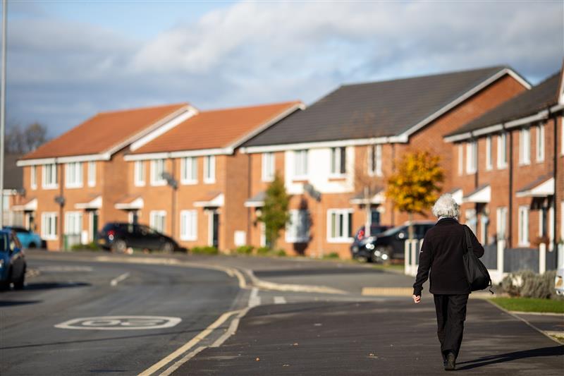 Someone walking on a quiet neighbourhood road with rows of new‑build homes.