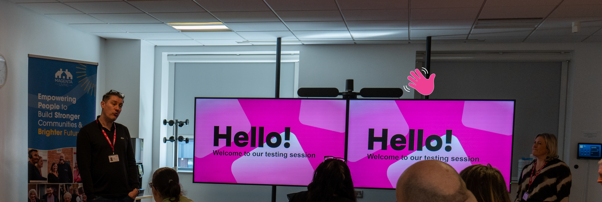 People seated in a meeting room watch a presentation on two screens reading “Hello! Welcome to our testing session.”