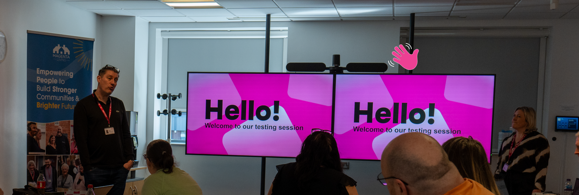People seated in a meeting room watch a presentation on two screens reading “Hello! Welcome to our testing session.”