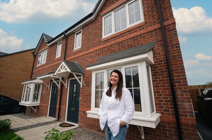 Customer standing outside a modern red‑brick family home with a front garden and driveway.