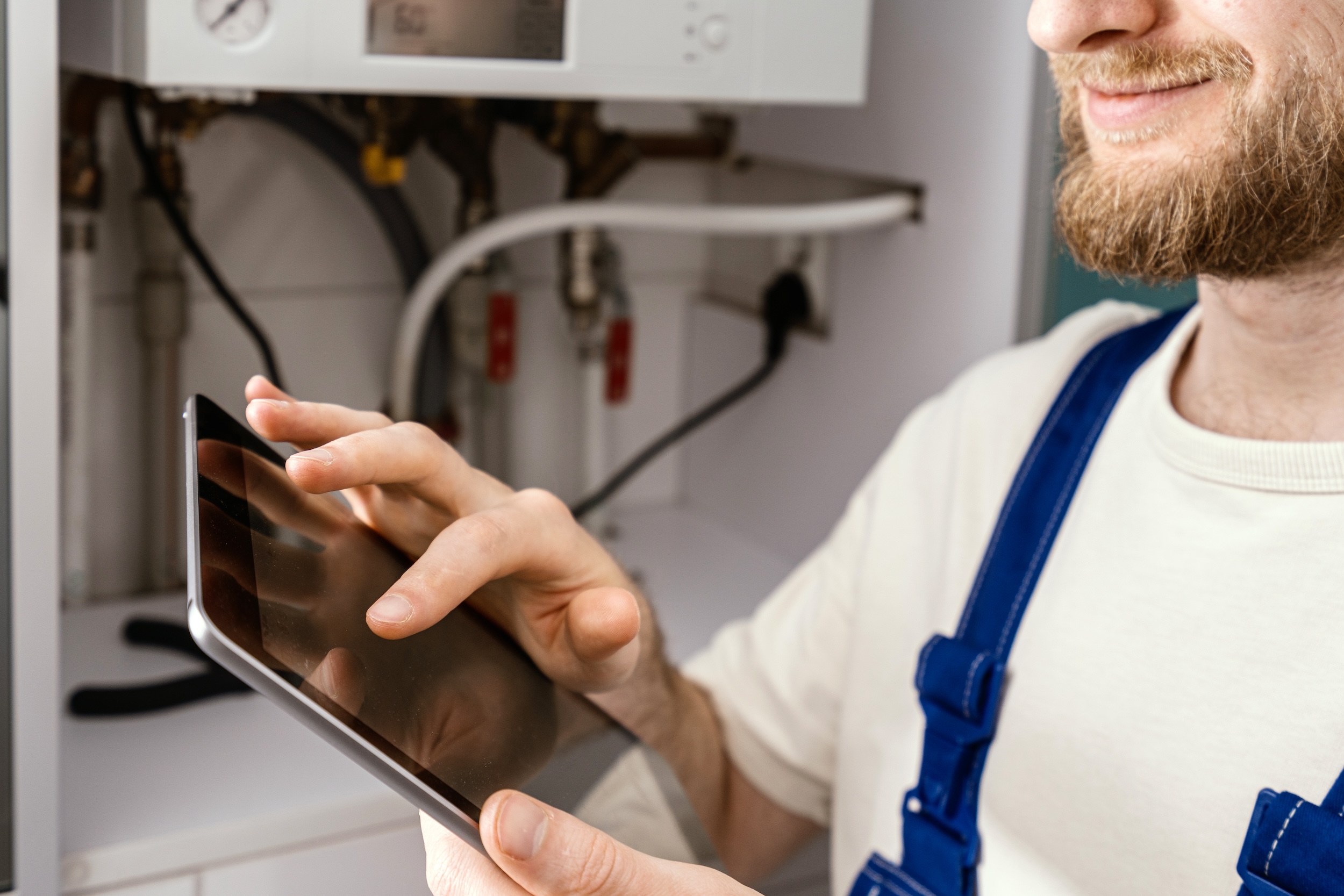 Technician inspecting a household boiler and recording information on a tablet.