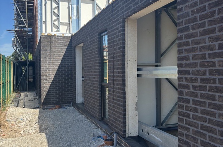 A row of new homes under construction at Sandbank Point in West Kirby. The image shows brick-clad external walls, window openings and prefabricated structural panels being assembled on site, with scaffolding visible alongside the buildings. The development will provide 14 carbon zero homes built using modern methods of construction.