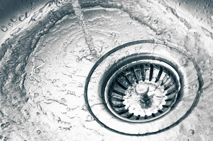 Water flowing into a stainless steel sink, swirling around the drain.