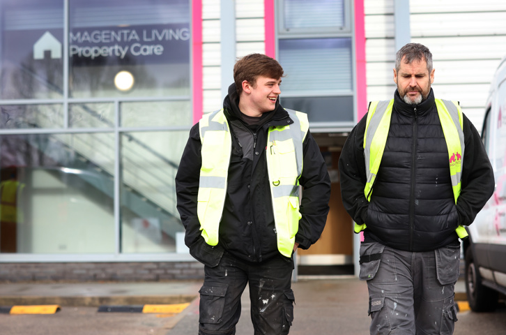 Two property care colleagues in high‑visibility vests walking outside a Magenta Living building.