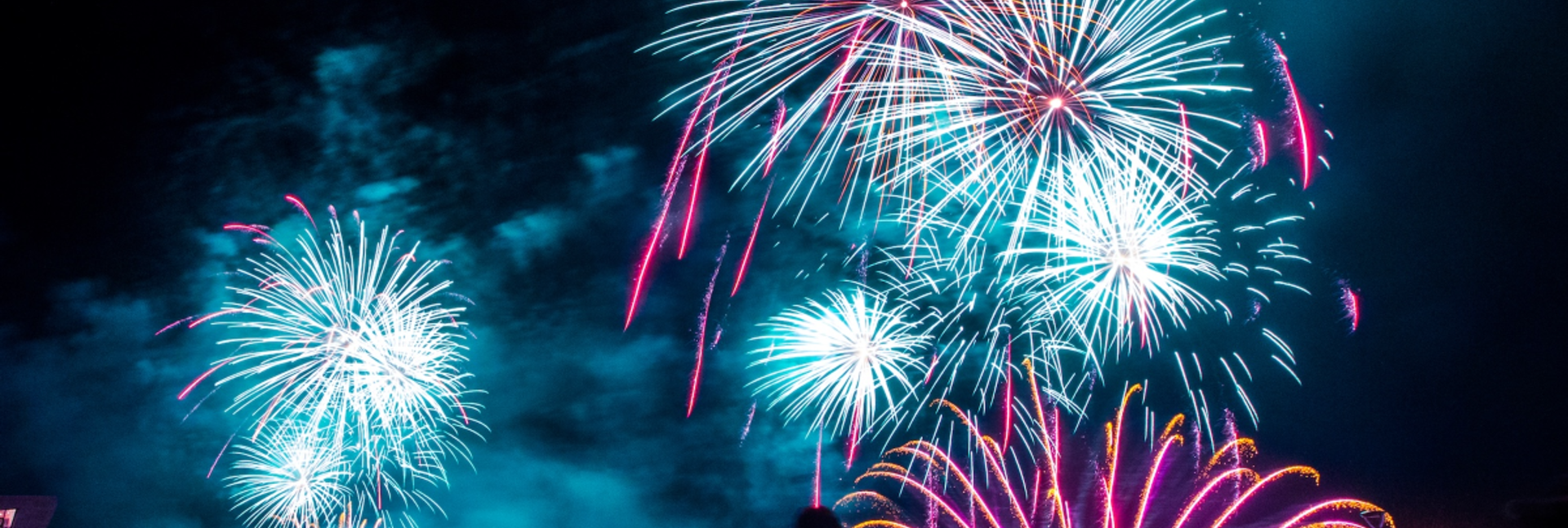 Bright fireworks bursting in the night sky above a crowd at an outdoor event.