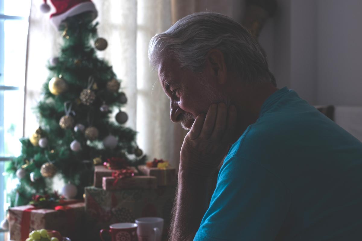 A person sitting indoors near a decorated Christmas tree and wrapped presents