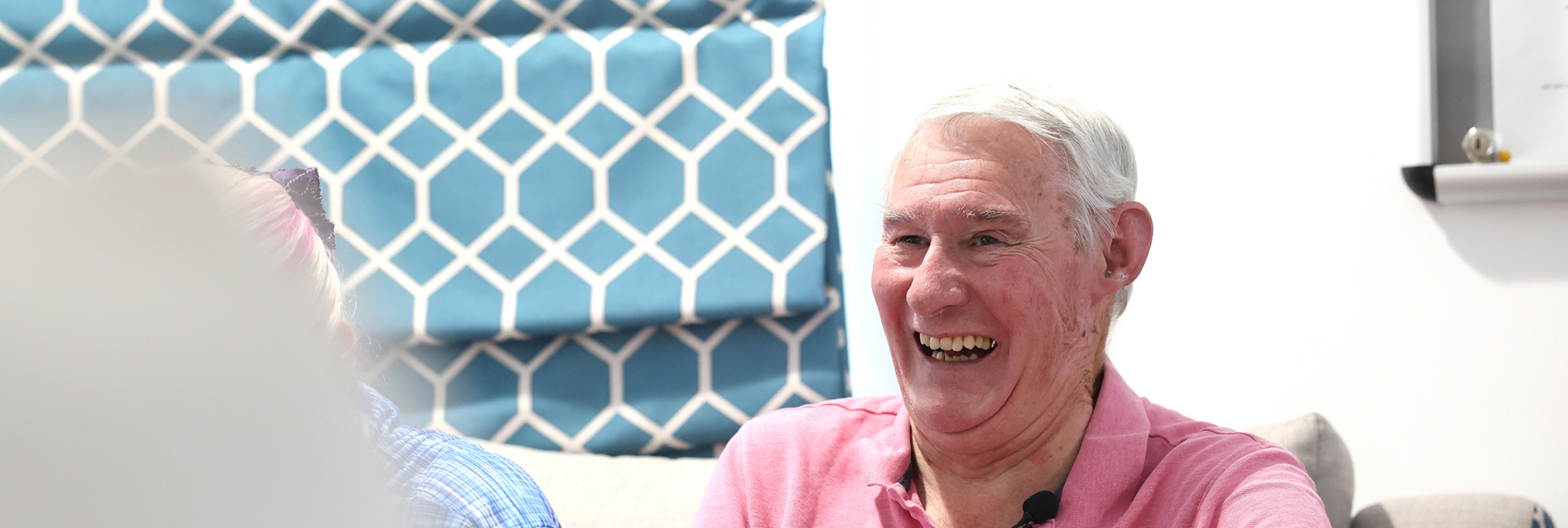 Person wearing a pink polo shirt seated in an armchair during a group discussion in a community setting.