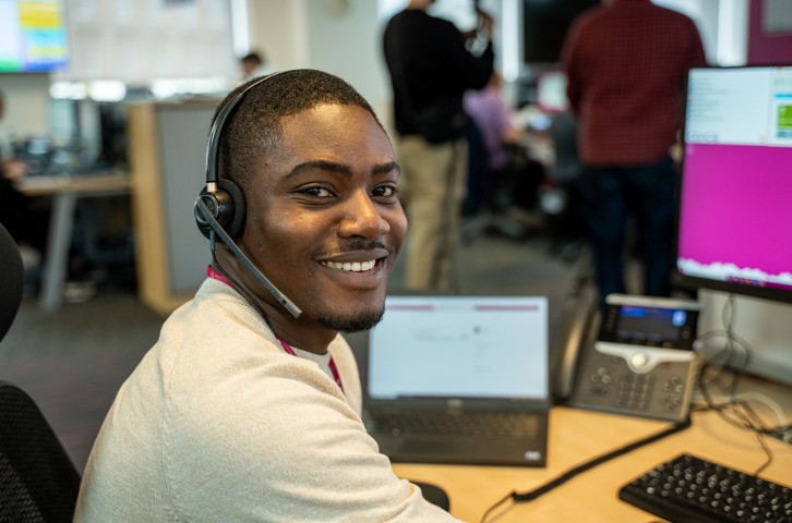 Male with headset on smiling at the camera with a computer screen in the background