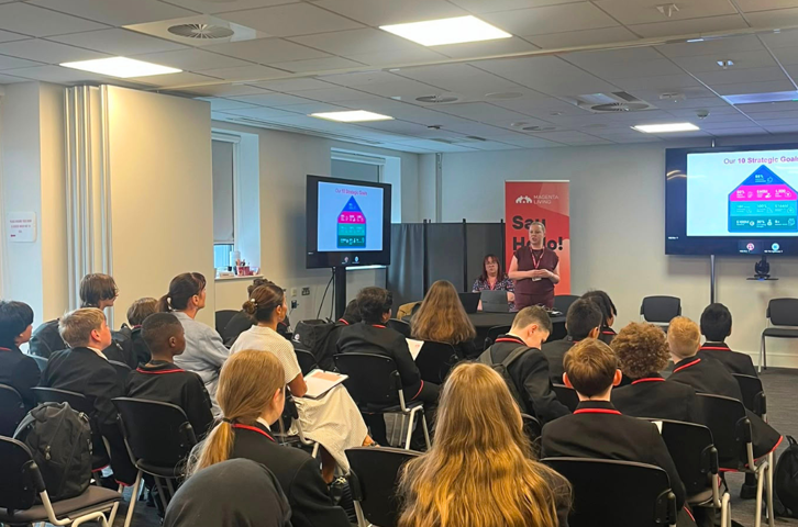 Birkenhead Park School students listen to a presentation during a visit to Magenta Living, with a speaker addressing the room from the front.