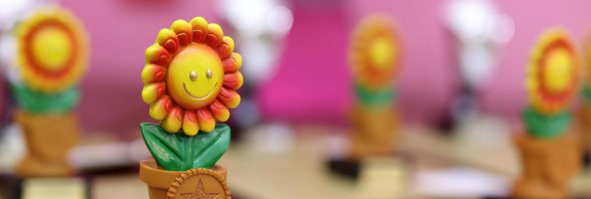 A colourful sunflower‑shaped award trophy displayed on a table with other trophies in the background.