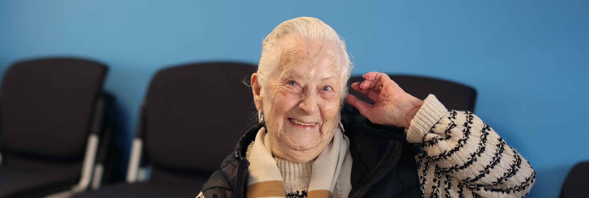 A person sitting at a table in a community room, holding a snack with a plate of food in front of them.