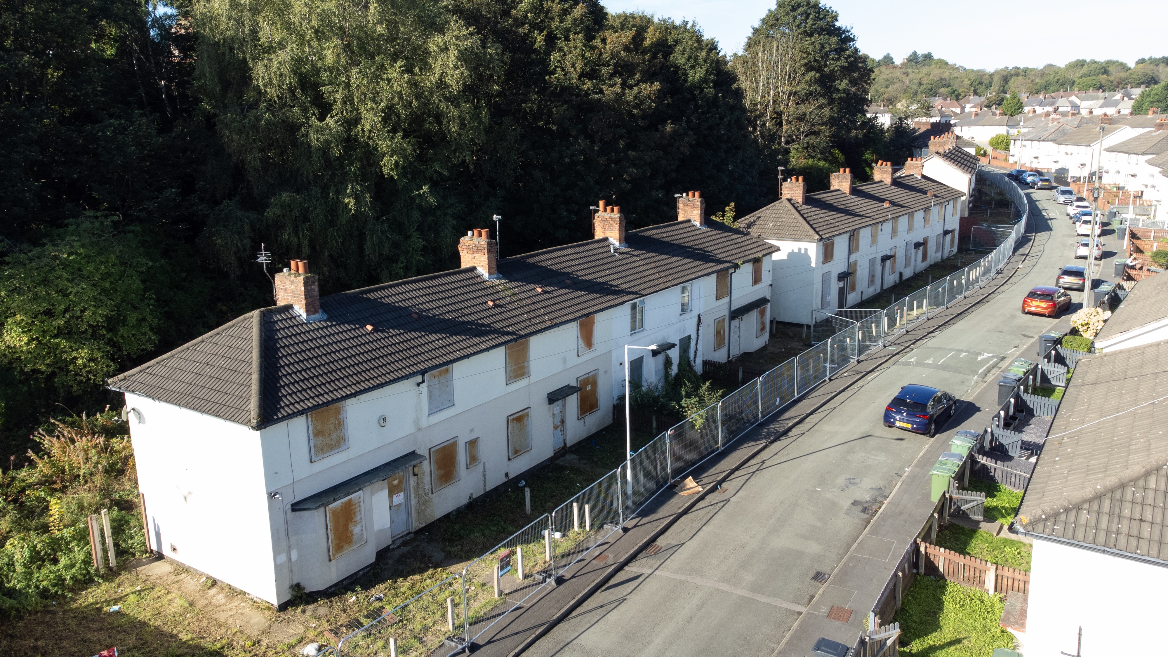 A row of empty, boarded‑up homes on a curved residential street, fenced off for safety.