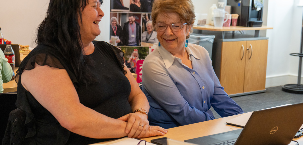 Two people sit at a table smiling and looking at a laptop during the customer testing session.