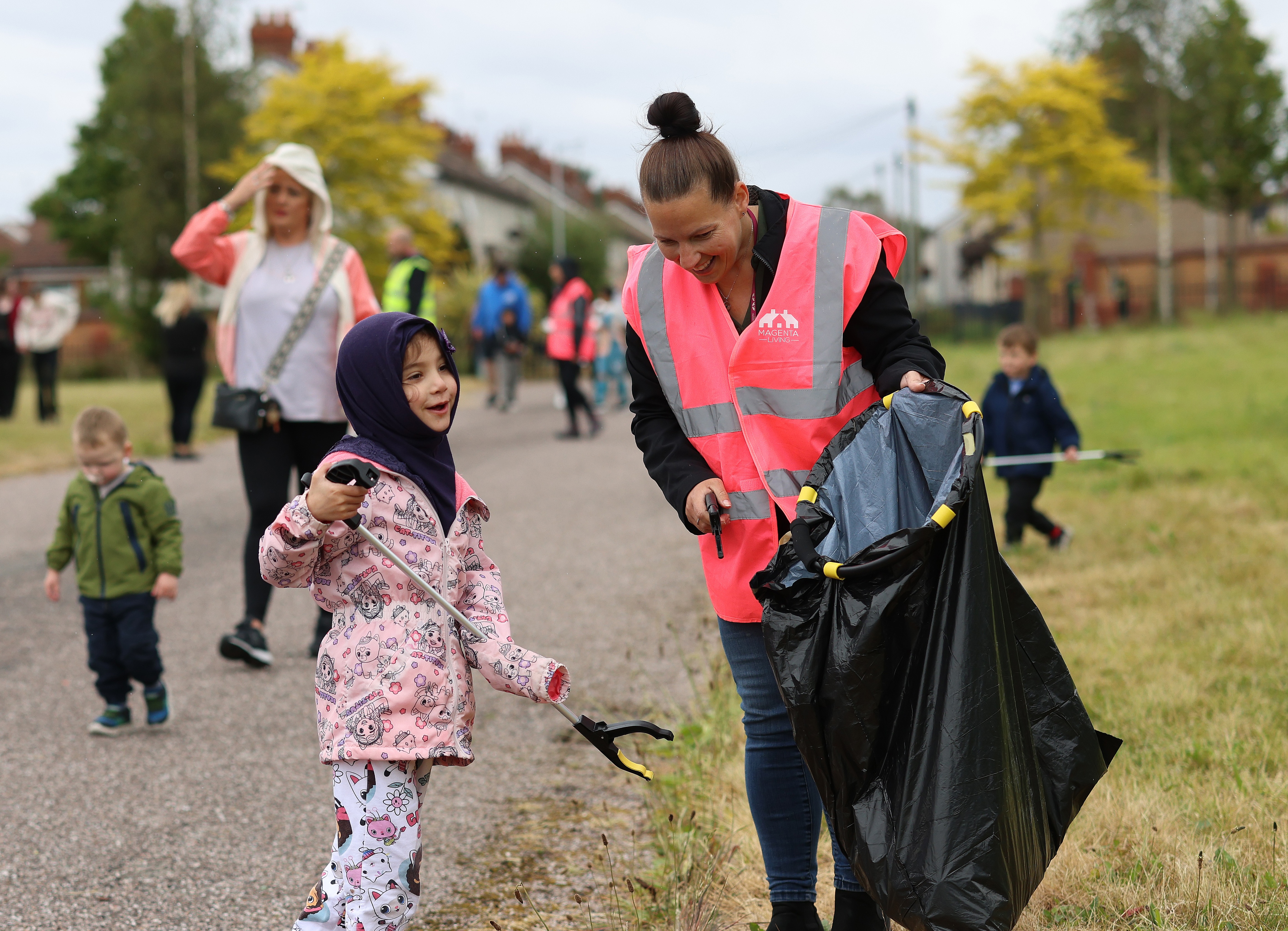 A child and an adult in high‑visibility vests taking part in a community litter‑pick, using grabbers and a bin bag.