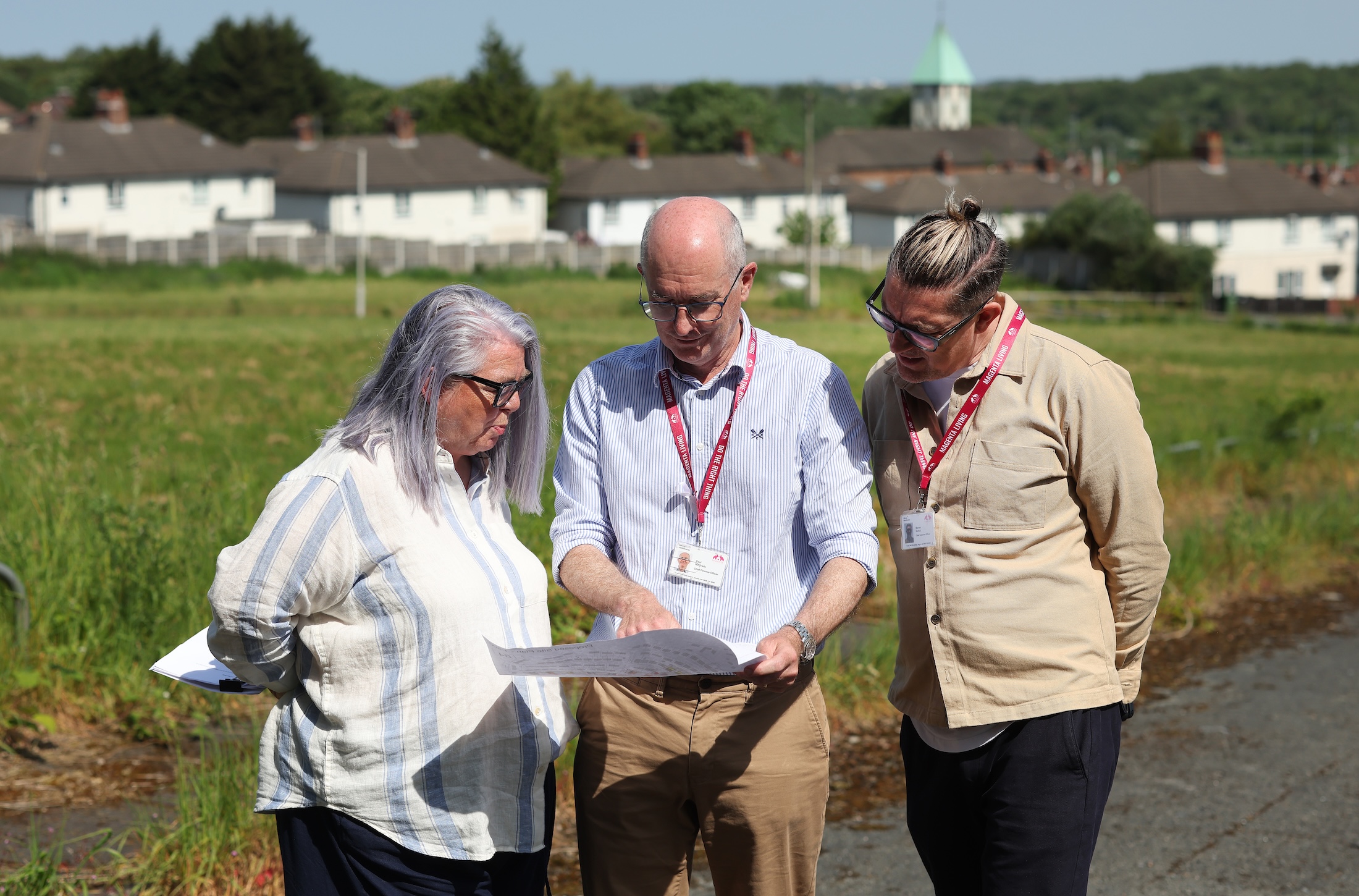 Paul McGrady, Magenta Living Chief Finance Officer looking at house building plans with colleagues in a field with homes in the background.