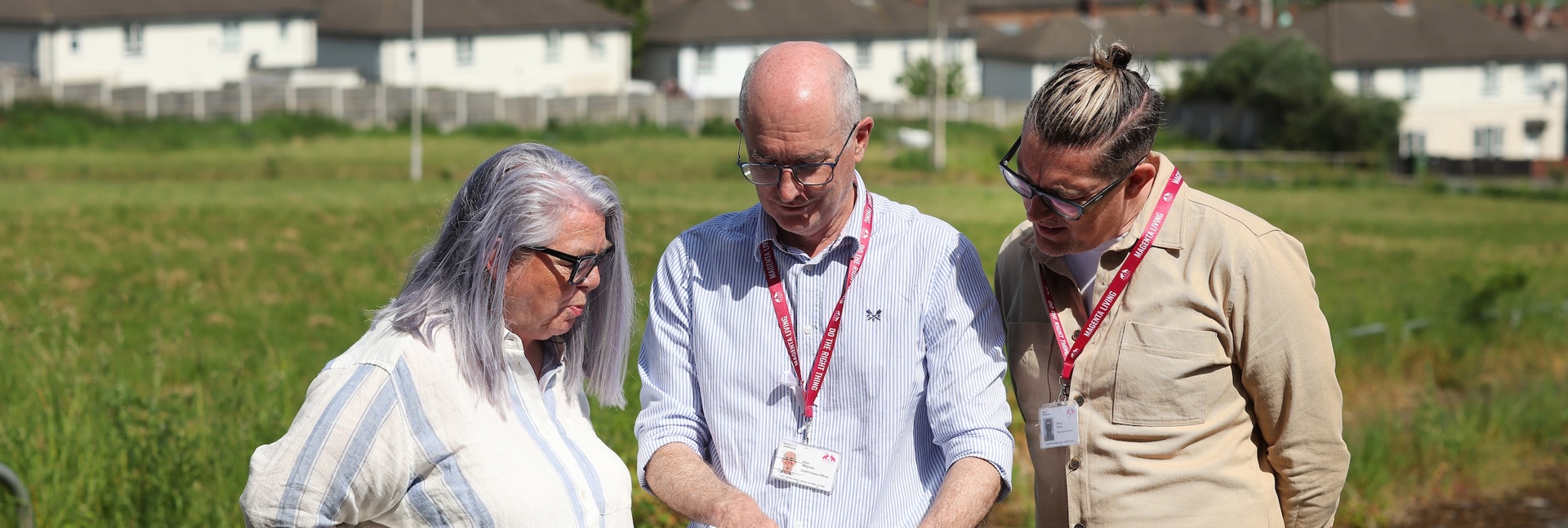 Paul McGrady, Magenta Living Chief Finance Officer looking at house building plans with colleagues in a field with homes in the background.