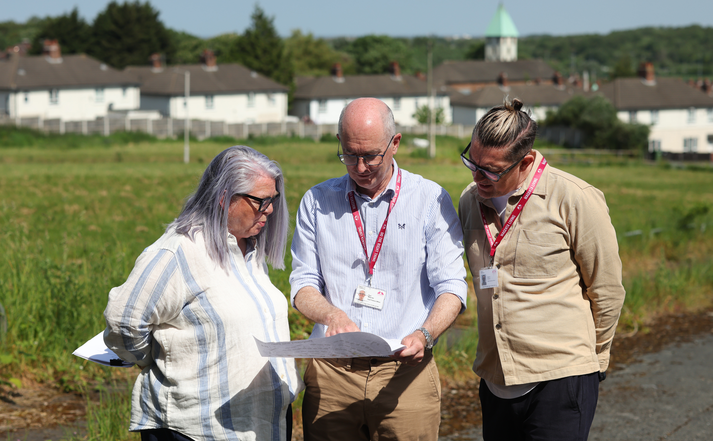 Paul McGrady, Magenta Living Chief Finance Officer looking at house building plans with colleagues in a field with homes in the background.