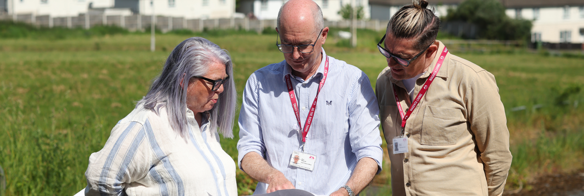 Paul McGrady, Magenta Living Chief Finance Officer looking at house building plans with colleagues in a field with homes in the background.