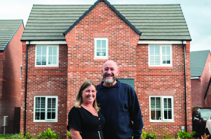 A pair of customers posing in front of a modern red‑brick house on a residential street.