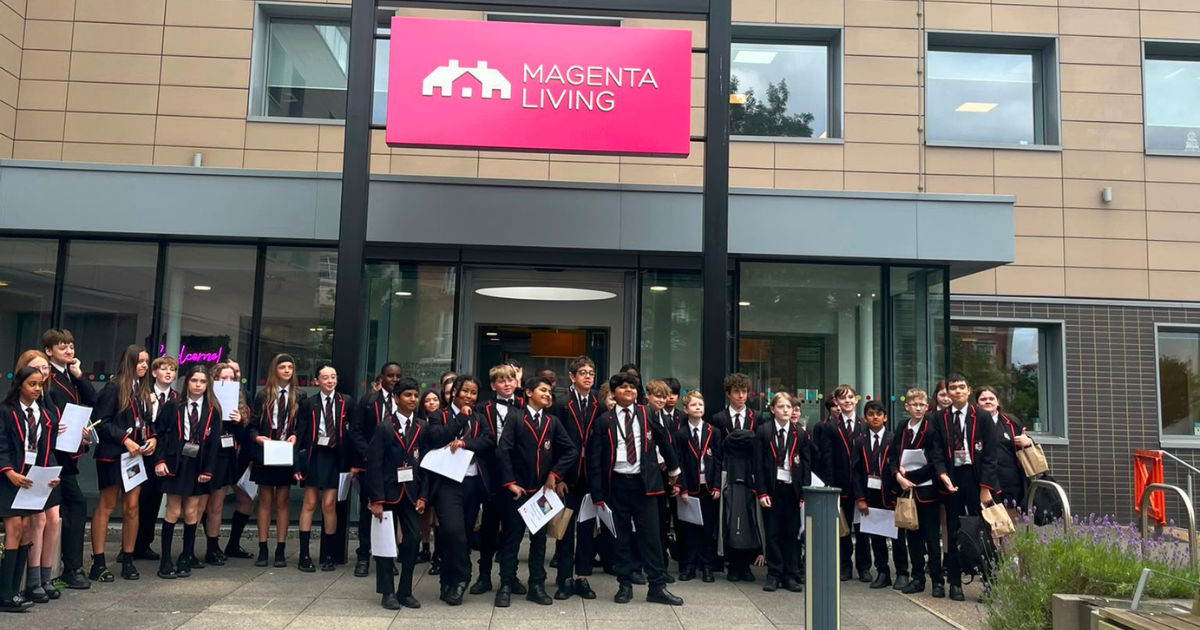 Birkenhead Park School students stand outside Magenta Living’s office building during an educational visit, holding worksheets as they stand for a group photo.