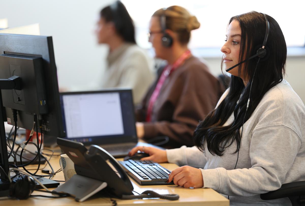 Colleagues working at computer desks in a customer service office, wearing headsets.