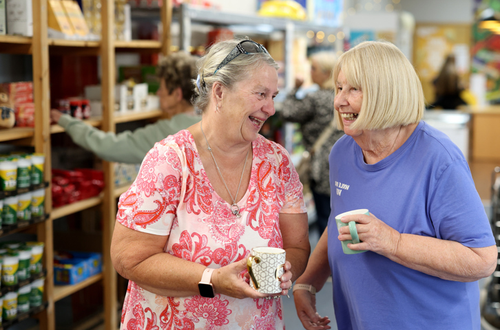 Two people holding mugs chat together in a welcoming community space.