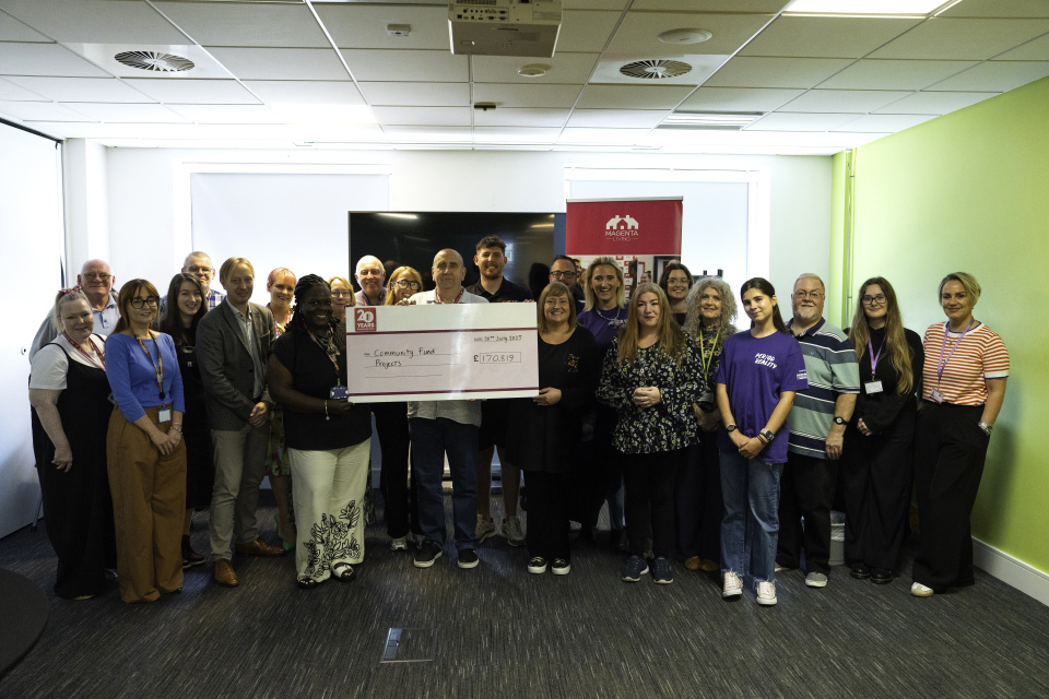 A large group of people standing together indoors holding an oversized cheque for a community fund projects.