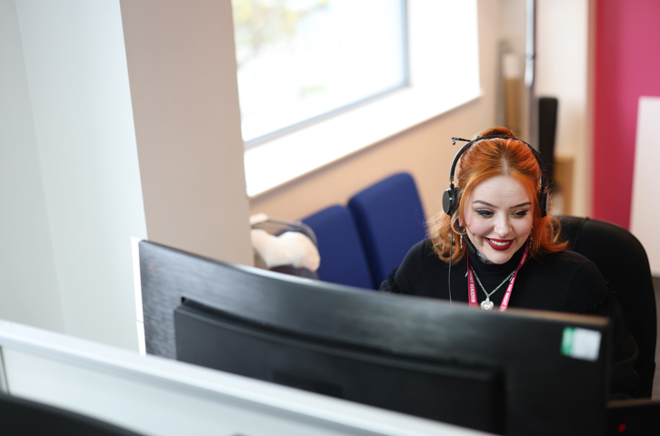 Colleague wearing a headset while working at a computer in a bright office.