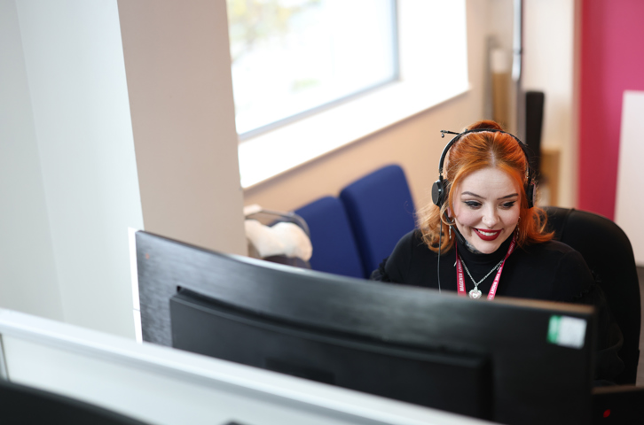 Colleague wearing a headset while working at a computer in a bright office.