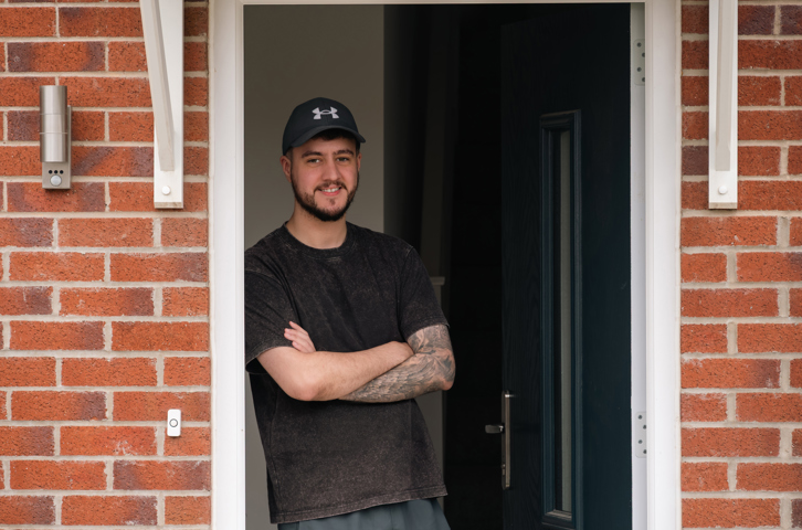 Customer standing in the doorway of a red‑brick home with arms crossed and the front door open behind them.