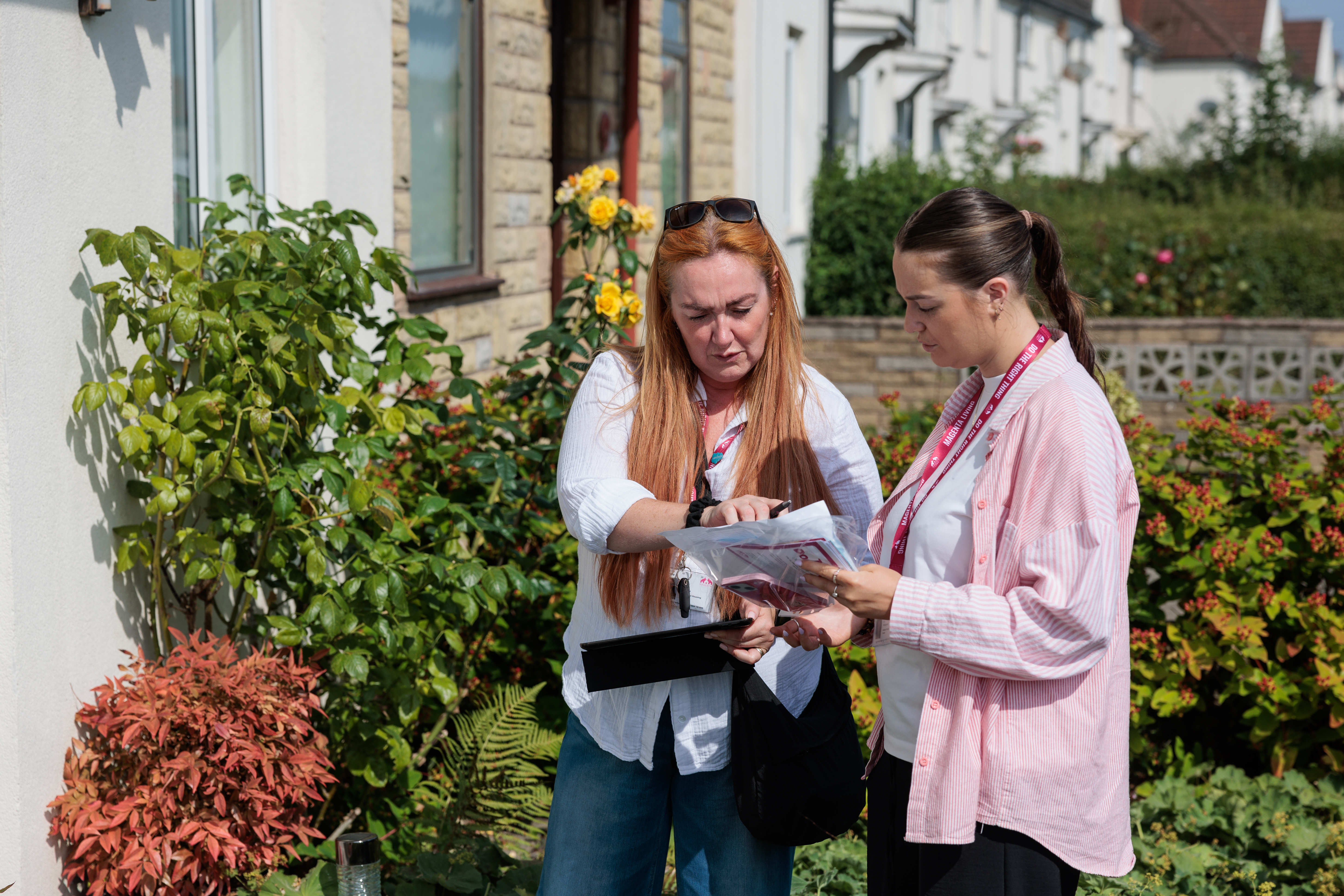 Two Magenta Living colleagues review paperwork together outside a property, surrounded by plants and flowers.