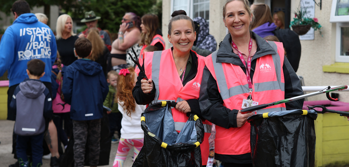 Community clean‑up volunteers in hi‑vis vests with litter‑picking equipment, with a crowd gathered in the background.