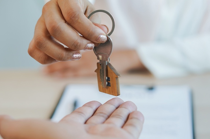 Hand passing a house key to another person.